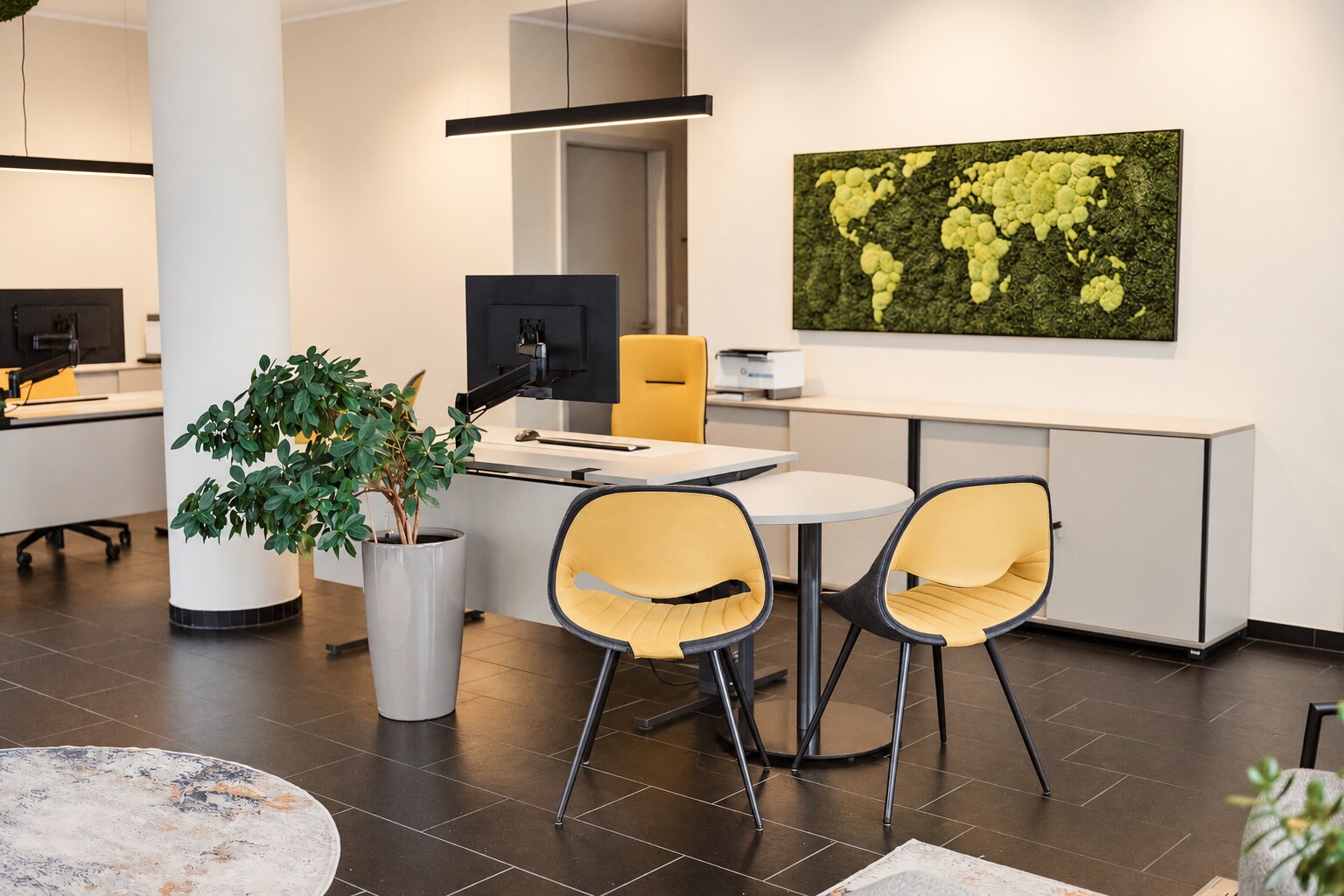 Einladender Beratungsplatz im Reisebüro auf dem Rodenhof mit gelben Stühlen, Pflanzen und grüner Weltkarte an der Wand.